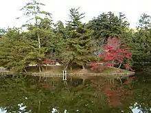 Île verdoyante au milieu d’un lac, avec un torii rouge.