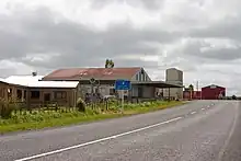 Quelques bâtiments bas au bord d'une route avec un panneau représentant une pompe à essence et le texte.