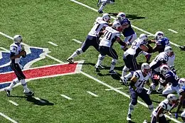 Tom Brady balle en main sur un terrain de football américain.