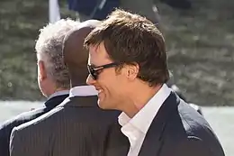 Tom Brady, de profil au premier plan, en costume et avec des lunettes de soleil.