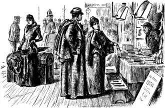 Gravure. Jeunes mariés devant l'étal de livres d'une gare ; la dame pointe du doigt le livre qu'elle convoite.