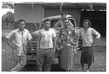 Photo en noir et blanc montrant 5 jeunes hommes polynésiens posant devant une voiture