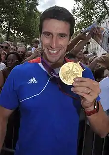 Photographie en couleurs d'un sportif exhibant sa médaille d'or.