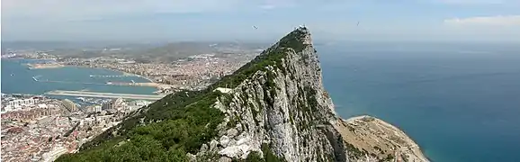 À l'avant-plan le Rocher, avec à l'est des falaises subverticales et à l'ouest des pelouses moins inclinées ; au fond, la presqu'île