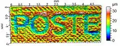 Micro-topographie d'un timbre-poste français d'usage courant (détail) montrant l'épaisseur d'encre obtenue par le procédé de taille-douce. Les caractères « POSTE » apparaissent sur le timbre en blanc sur fond rouge, et correspondent donc à une absence d'encre. La mesure a été réalisée à l'aide d'un profilomètre, et la fausse couleur représente l'altitude microscopique selon la légende figurant à droite.