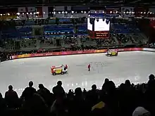 Une patinoire vue du haut des gradins. Sur la glace, deux surfaceuses.