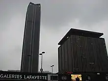 À l’emplacement de l’ancienne gare Montparnasse, l’« Ensemble immobilier tour Maine-Montparnasse », vu depuis le boulevard du Montparnasse. À gauche, en retrait, la tour Montparnasse elle-même, à droite le « bâtiment C » ou « Centre international du textile ». Le centre commercial Montparnasse Rive Gauche, qui accueillit entre autres, jusqu'en 2019, les Galeries Lafayette Montparnasse, est aménagé à la base de cet ensemble.