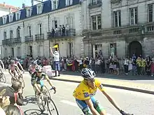 Photo prise à Périgueux représentant six cyclistes avec à leur tête le maillot jaune, lancés dans une rue à l'occasion du passage du Tour de France 2007 à Périgueux. Au second plan, la foule massée sur le trottoir applaudit.