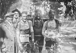 Trois cyclistes posant à l'arrivée, se tenant par l'épaule, à côté d'hommes en costume.