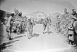 Cyclistes au sommet d'un col, sur une route empierrée, l'un sur son vélo, l'autre marchant à côté de sa bicyclette.