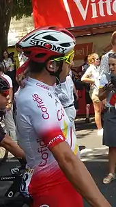 Photo d'un homme de profil, assis sur son vélo et portant un casque, des lunettes de soleil et une oreillette.