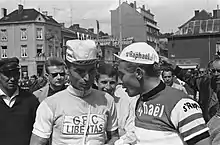 Photographie montrant deux cyclistes en conversation, entourés par la foule, au départ d'une course.