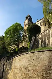 Photographie en contre-plongée d'une tour et son cadran en arrière plan. Partie de remparts au premier plan.