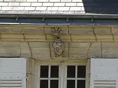 Photographie en couleurs du linteau d'une fenêtre décoré d'une sculpture de tête féminine.