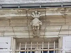 Photographie en couleurs du linteau d'une fenêtre décoré d'une sculpture de tête féminine.