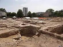 Vue de la base d'un base arasé au niveau du sol et portant une maçonnerie en exèdre.