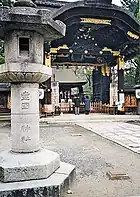 Photo couleur d'une porte en bois laqué noir d'un sanctuaire, avec une lanterne en pierre au premier plan.