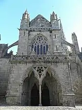 Une photo de façade d'église à deux niveaux, avec un grand porche central et au-dessus une grande baie à lancettes