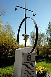 Photographie d'une stèle en pierre surmontée d'une roue de vélo et d'un guidon en fer.