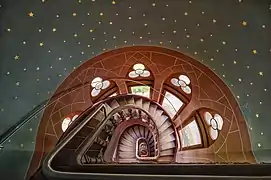 Vue plongeante dans un colimaçon d'escalier entouré d'étoiles peintes et de fenêtres l'inondant de lumière.