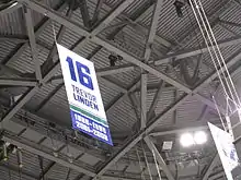 Photographie couleur de la bannière numéro 16 accrochée sous le plafond de l'arena.