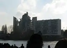 Une foule observe, sur la rive opposée de la Loire, un bâtiment d'une quinzaine d'étages s'effondrant.