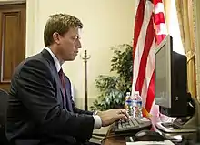 Un homme en costume avec une cravate rouge, de profil, tapotant sur un clavier d'ordinateur dont il regarde l'écran.