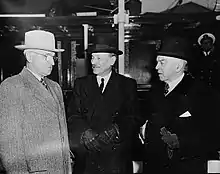 photographie en noir et blanc de trois hommes debout et en conversation.