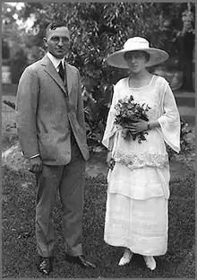 Photographie de mariage de Truman en costume gris et son épouse portant une robe et un chapeau blanc et tenant un bouquet de fleurs
