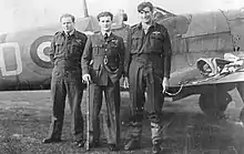 Photographie en noir et blanc de trois hommes posant devant un avion.