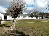 Photographie en couleurs d'un long bâtiment montrant un alignement de fenêtres avec une grande cour au premier plan.