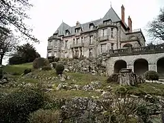 Photographie en couleurs de la façade d'un château avec un jardin de rocaille au premier plan.