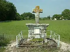 Photographie en couleurs d'une croix sur son support, le tout en pierre au milieu d'un champ.