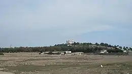 Vue d'une plaine avec au fond une colline avec un grand édifice religieux et sur la gauche un minaret à l'arrière-plan.