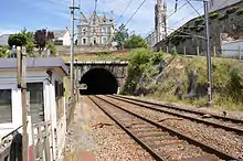 depuis le passage à niveau, une vue du tunnel dont on aperçoit la sortie et, au-dessus, la maison ancienne et l'église