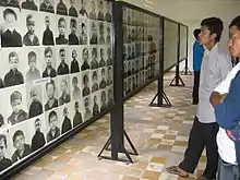 Photographie couleur d'un homme regardant des portraits d'enfants fixés sur un mur.