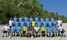 Photographie de l'équipe des Tuvalu : 28 hommes sont de face, debouts, souriants, sur trois rangs, sur la plage, sous des palmiers.