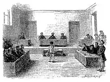 Grande salle, estrade avec trois hommes assis, rangées de bancs latéraux, garçon s'avançant vers le jury.