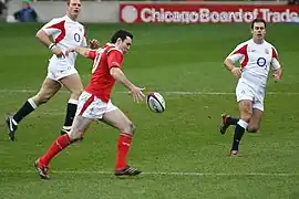 Un joueur en maillot rouge s'apprête à taper le ballon au pied devant deux joueurs en maillot blanc