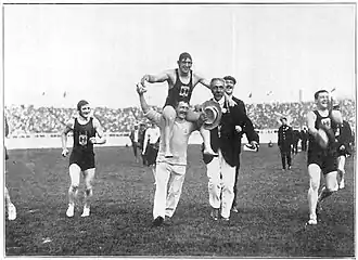 phographie noir et blanc : des hommes courent dans un stade ; l'un d'entre eux est porté en triomphe
