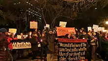 Dans la nuit, en milieu urbain, des dizaines de manifestants brandissent des bougies et d'autres sources de lumière ainsi que des pancartes contre Keystone XL.