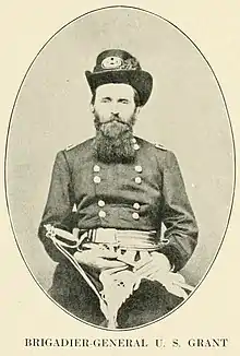 Photographie d'un homme barbu en uniforme militaire. Il est assis et tient son sabre dans ses mains.
