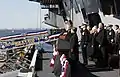 Le président George W. Bush, son épouse Laura Bush durant l'exécution de l'hymne national américain lors de la cérémonie de l'armement de l'USS George H. W. Bush (CVN 77) baptisé en l'honneur de son père, situé derrière lui au côté notamment du vice-président Dick Cheney