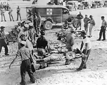 Photo en noir et blanc de blessés transportés sur des civières.