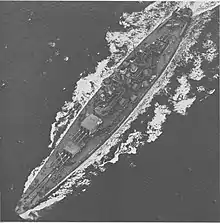 Photographie aérienne d'un navire avec trois tourelles triples, deux à l'avant et une à l'arrière