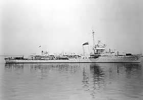 Photographie en noir et blanc d'un long navire de guerre, la proue pointant vers la droite de l'image.