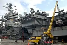 Le porte-avions à quai, en train de recevoir du matériel par grue.