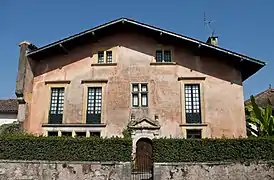 Photographie d'une maison à trois étages et au toit à deux pans, aux murs roses.