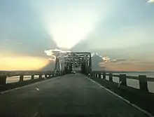 Vue d'une route sur un pont. La photo est prise au coucher ou lever de soleil.