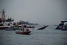 L'avion, au centre de l'image, à peine visible à mesure qu'il coule dans le fleuve, est entouré par plusieurs navires de secours.